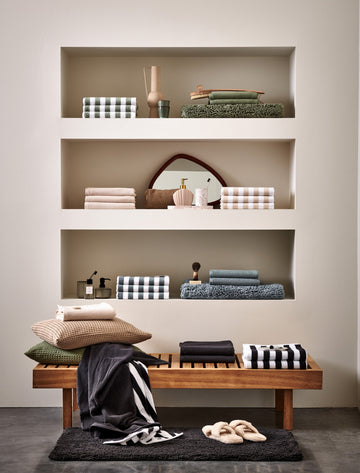 VERONA STRIPES badgoed | pearl blue Een shot van een kast met handdoeken en badmatten in zowel strepen en effen kleuren. Voor de kast staat een bankje met daarop ook handdoeken en sierkussens