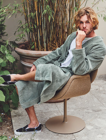 ANTONIO badjas | olive Man die in de tuin zit op een stoel met een badjas aan met strepen in groen en wit