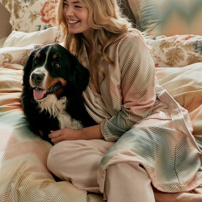 ROMANCE dekbedovertrekset | cream tan Vrouw op bed met een hond op een bed met een dekbedovertrek met een zig zag print en een badjas aan met een zig zag print