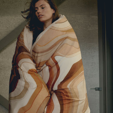 SPIRIT dekbedovertrekset | multi Een vrouw met een dekbedovertrek om haar heen geslagen in een print met bruine en oranje kleuren