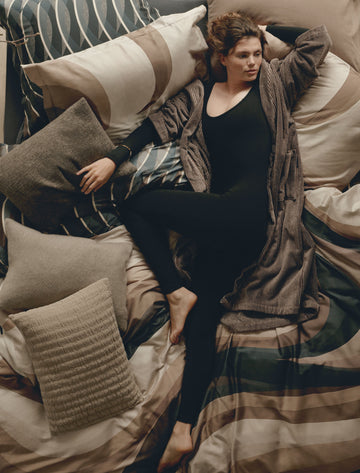 ESPRESSO LANE dekbedovertrekset | multi Topshot van een vrouw die op een bed ligt met een bruine badjas aan op een bed met dekbedovertreksets in organische vormen in bruine en donkergrijze kleuren