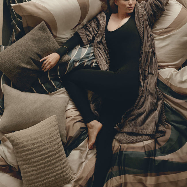 ESPRESSO LANE dekbedovertrekset | multi Topshot van een vrouw die op een bed ligt met een bruine badjas aan op een bed met dekbedovertreksets in organische vormen in bruine en donkergrijze kleuren