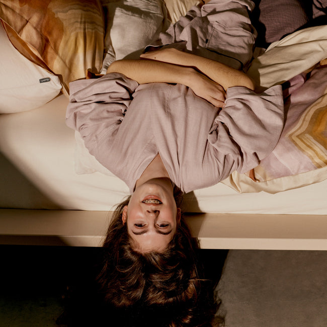 MIMOSA dekbedovertrekset | multi Een jonge meid ondersteboven in bed met een lila badjas aan