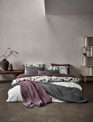 OLIVE dekbedovertrekset | multi een bed in een rustige omgeving met een dekbedovertrek in een licht groene kleur met olijftakken en een dekbedovertrek in een paars bruine kleur en spreien op het bed in een grijze en paarse kleur
