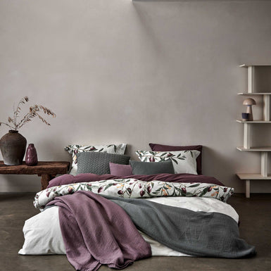OLIVE dekbedovertrekset | multi een bed in een rustige omgeving met een dekbedovertrek in een licht groene kleur met olijftakken en een dekbedovertrek in een paars bruine kleur en spreien op het bed in een grijze en paarse kleur