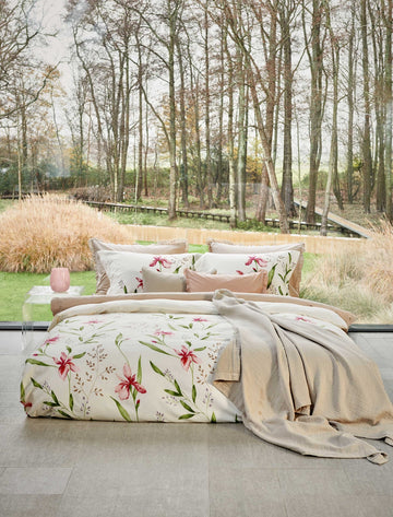 SERENE FLOWER dekbedovertrekset | offwhite een bed in een rustige omgeving. Op het bed ligt een dekbedovertrek met roze bloemen en groene bladeren en een beige sprei