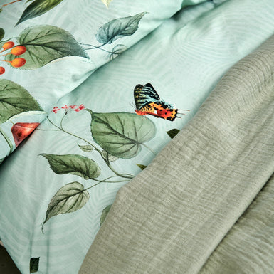 FRUIT GARDEN dekbedovertrekset | light green detail shot van een dekbedovertrek met vruchten, bladeren en vlinders op een lichtgroene achtergrond en een plaid in groen