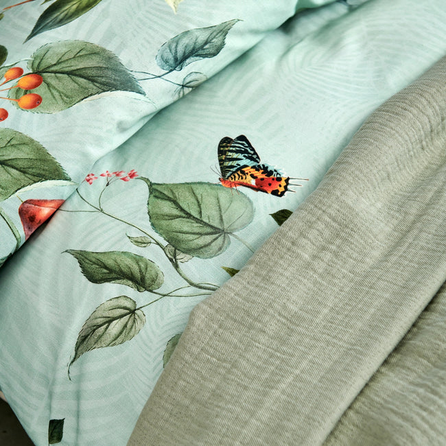 FRUIT GARDEN dekbedovertrekset | light green detail shot van een dekbedovertrek met vruchten, bladeren en vlinders op een lichtgroene achtergrond en een plaid in groen