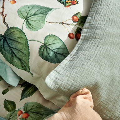 FRUIT GARDEN dekbedovertrekset | cream tan detail shot van kussens in een groene en roze kleur en een kussen met bladeren en vlinders op een beige achtergrond