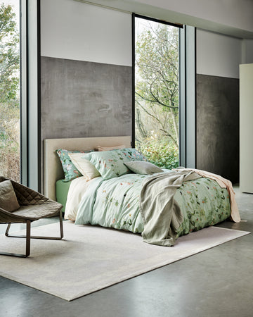 GARDENIA dekbedovertrekset | smoke green Een bed met een groen dekbedovertrek in een rustige omgeving