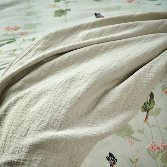 GARDENIA dekbedovertrekset | smoke green detail shot van een groen plaid en een dekbedovertrek met bloemen en vlinders