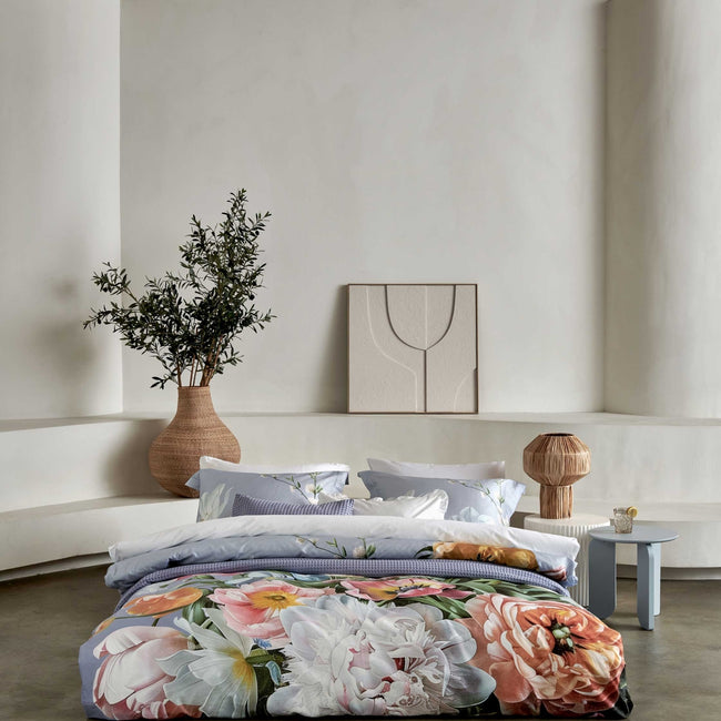 FLEUR FESTIVE dekbedovertrekset | lavender blue Fleur Festive lavender blue dekbedovertrek heeft hele grote bloemen in lichte pasteltinten in blauw, roze en oranje schakeringen op een blauw / paarse achtergrond. De achterkant van het dekbedovertrek is effen beige. De kussens hebben aan beide kanten een paar bloemen en een bloesemtak.