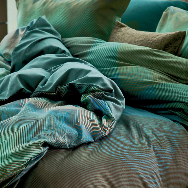 ZIGGY dekbedovertrekset | sage green detail shot van een bed met grafische dekbedovertrekken in groene en blauwe kleuren