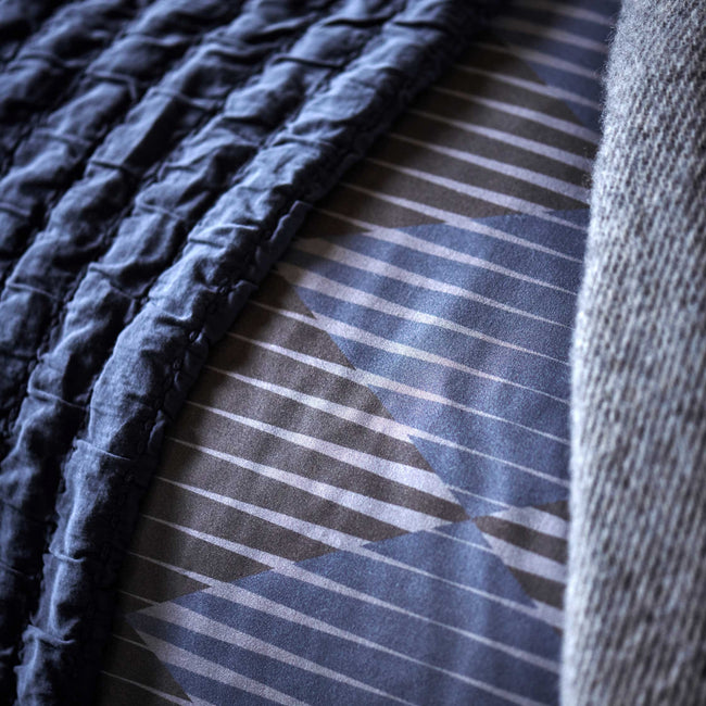 CHARGE dekbedovertrekset | oceanview detail shot van een dekbedovertrek met grafische print in grijze en donkerblauwe kleuren en een plaid in een donkerblauwe kleur