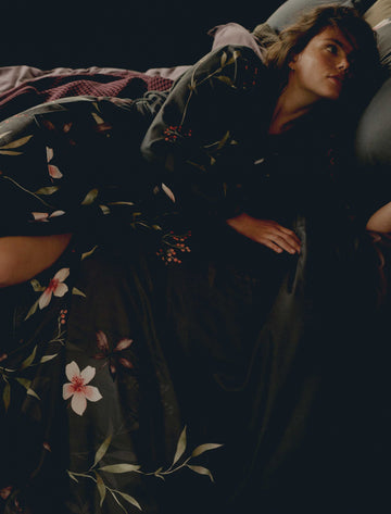 MYSTERY dekbedovertrekset | multi Een vrouw die op een bed ligt met een badjas aan met bloemen in een off black kleur