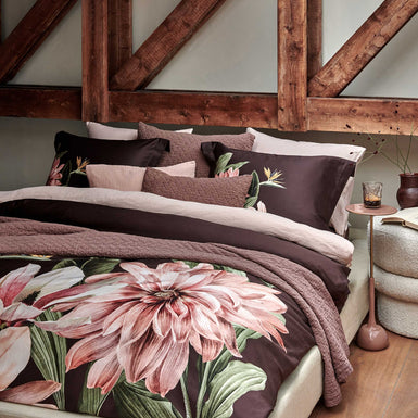 PARADISE BLOOM dekbedovertrekset | dark chocolate Een bed met een dekbedovertrek in een bruine kleur met een grote roze bloem en een sprei en sierkussens in een bruine kleur