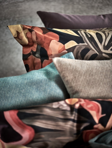 HOME BENEVENTO plaid | hazel detail shot van een bed met een kussensloop met bloemen en sierkussens in de blauwe en bruine kleuren