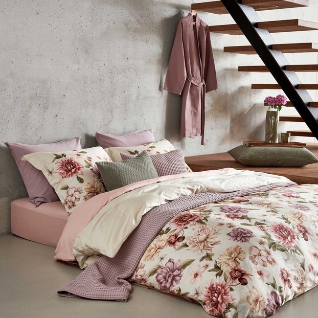 DYNAMIC dekbedovertrekset | multi Een bed in een rustige setting met een dekbedovertrek met rode, paarse en beige bloemen. Op het bed ligt een sprei in een lila kleur en in een groene kleur