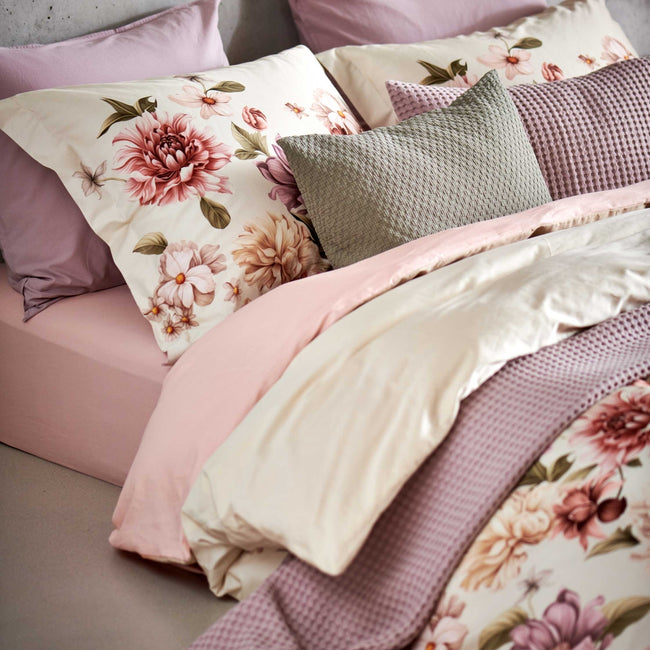 DYNAMIC dekbedovertrekset | multi detail shot van een dekbedovertrek in een beige kleur met roze, paarse en beige bloemen op het bed ligt een sprei en een sierkussen in een paarse kleur en een sierkussen in een groene thyme kleur
