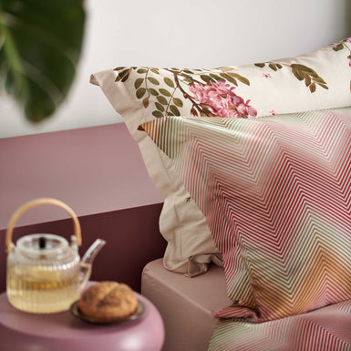 ROSE ACACIA dekbedovertrekset | cream tan detail shot van een hoofdkussen met zigzag print in roze, groen en oranje kleuren en een hoofdkussen met roze bloemen en groene bladeren