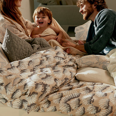 WAKE UP dekbedovertrekset | linen Een lachend stel in bed met een kind op een mooie zonnige ochtend