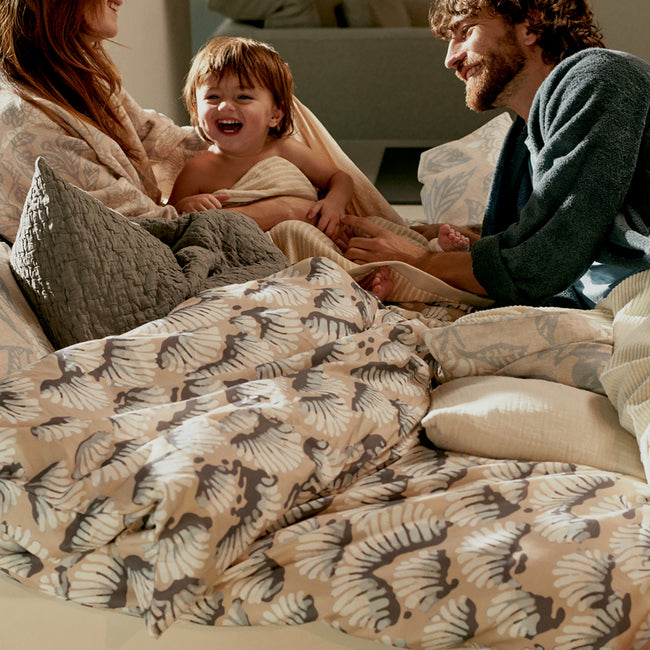 WAKE UP dekbedovertrekset | linen Een lachend stel in bed met een kind op een mooie zonnige ochtend