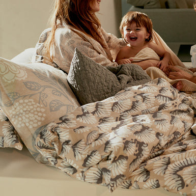 MARLY badjas | linen Een moeder met haar kind lachend in bed met een prachtig dekbedovertrek in rustige beige kleuren