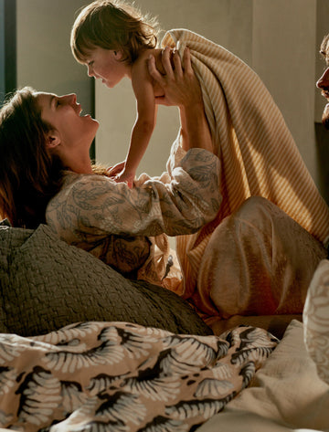 MARLY badjas | linen Een moeder met haar kind in bed lachend op een rustige zondag ochtend