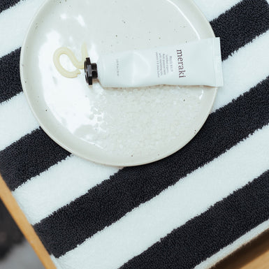 een detail shot van een zwart met wit gestreepte handdoek en daar bovenop een schaaltje met handcrème 
