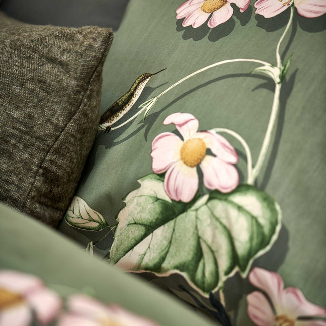 detail shot van een hoofdkussen in een groene kleur met een print van vogels en bloemen