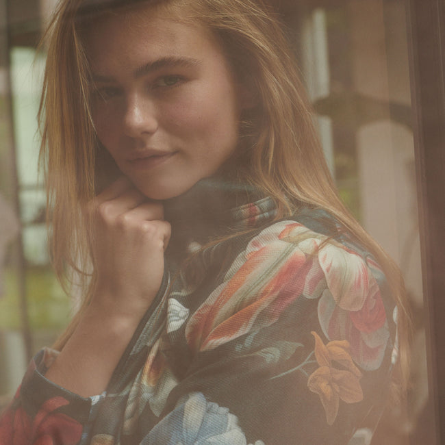 Een reflectie van een vrouw in een raam, ze draagt een bloemenprint badjas
