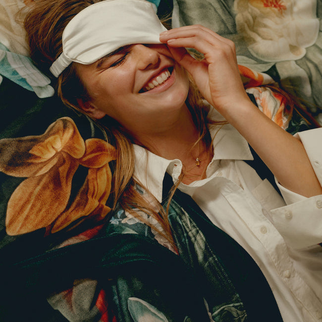 Een vrouw die op een bed ligt met een slaapmasker op in het wit en een dekbedovertrek in het blauw met bloemenprint