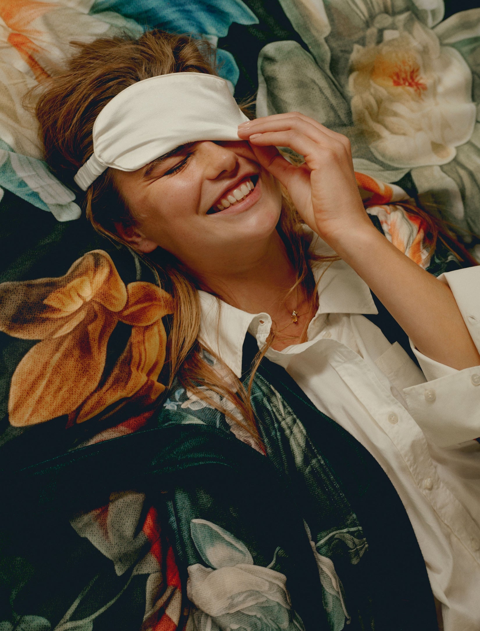 Een vrouw die op een bed ligt met een slaapmasker op in het wit en een dekbedovertrek in het blauw met bloemenprint