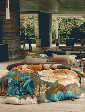 Een bed in een woonkamer met een groen dekbedovertrek met bloemen in gele en blauwe kleuren