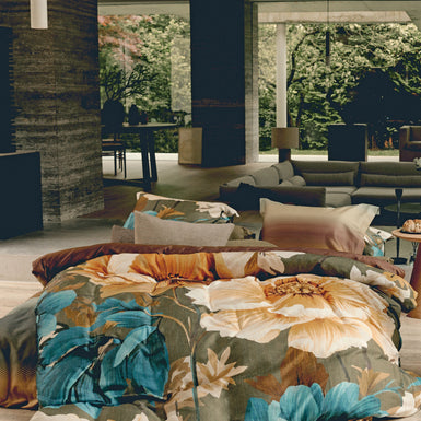 Een bed in een woonkamer met een groen dekbedovertrek met bloemen in gele en blauwe kleuren