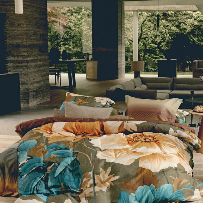 Een bed in een woonkamer met een groen dekbedovertrek met bloemen in gele en blauwe kleuren