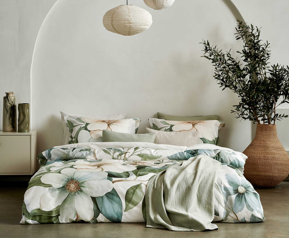 Een bed met een dekbedovertrek met groene bloemen en bladeren. Op het bed ligt een passend groen plaid