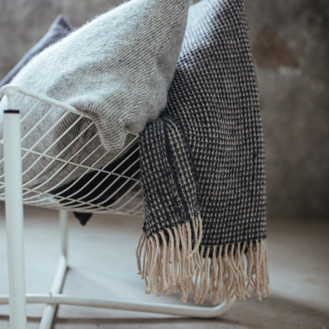 detail shot van een kussen van wol in en grijze kleur en een sprei