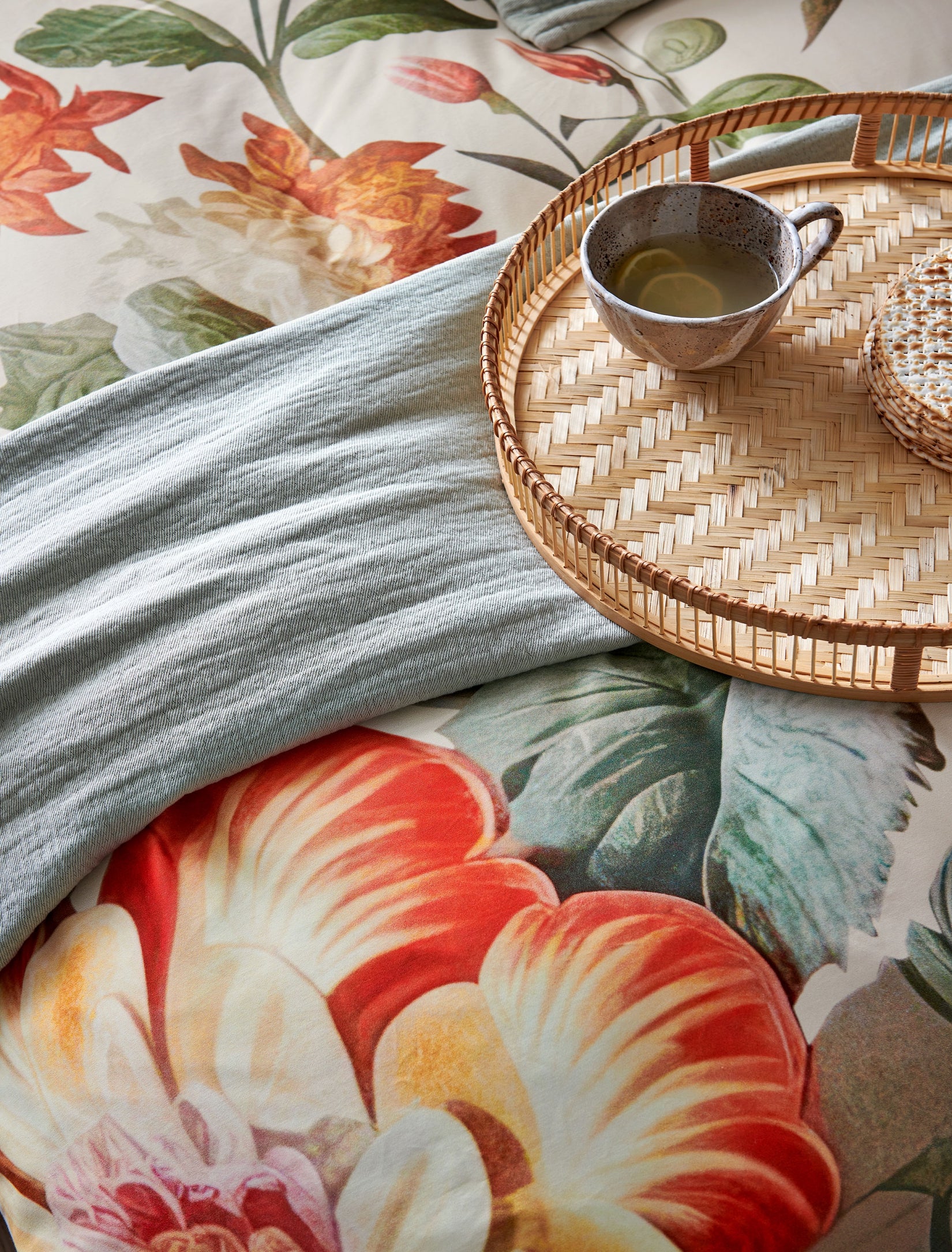 Detail van een dekbedovertrek met oranje bloemen, een plaid en een kopje thee