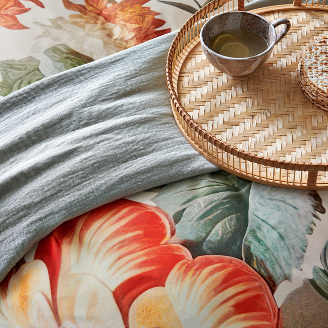 Detail van een dekbedovertrek met oranje bloemen, een plaid en een kopje thee