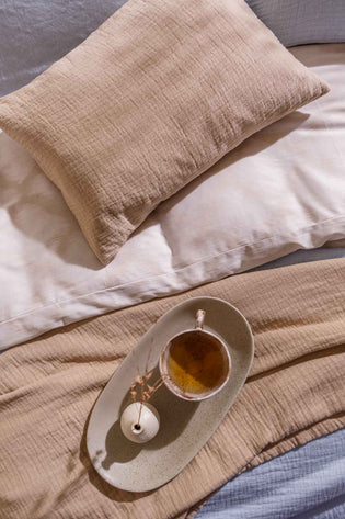 PURE 68 sprei | linen detail shot van een bed met een sierkussensloop in een linen kleur en een kopje thee op een bed