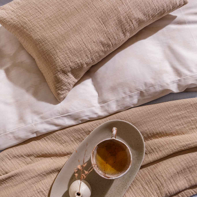 detail shot van een bed met een sierkussensloop in een linen kleur en een kopje thee op een bed