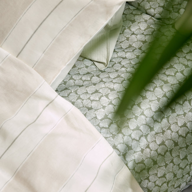 detail shot van een dekbedovertrek in beige met strepen en een dekbedovertrek met schelpen op een groene achtergrond