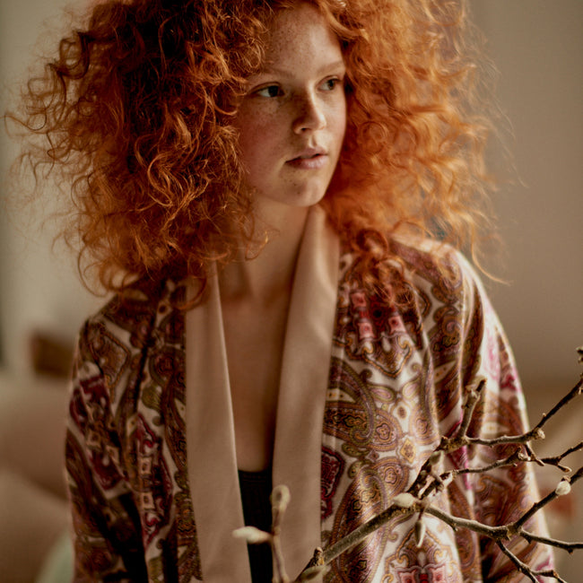 meisje met oranje haren in een badjas met oranje tinten en een paisley print