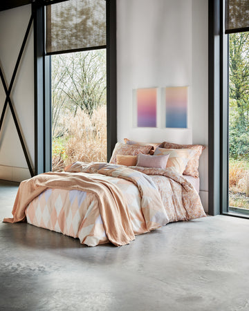 Een bed in een rustige setting met een dekbedovertrek in oranje en pasteltinten