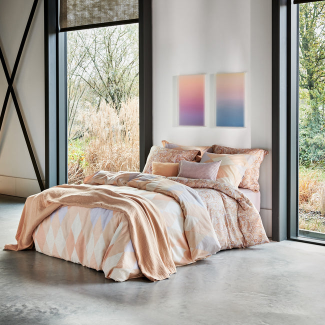 Een bed in een rustige setting met een dekbedovertrek in oranje en pasteltinten