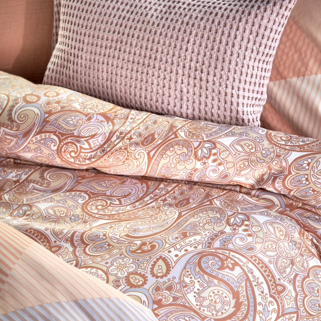 detail shot van een dekbedovertrek in een paisley print en een kussen met waffle structuur in lila en pastel oranje kleuren