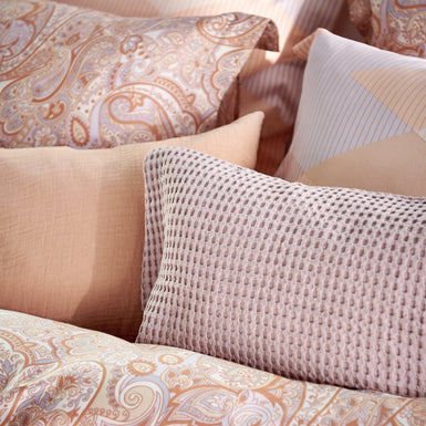 detail shot van een bed met kussens in oranje en lila pastel kleuren 