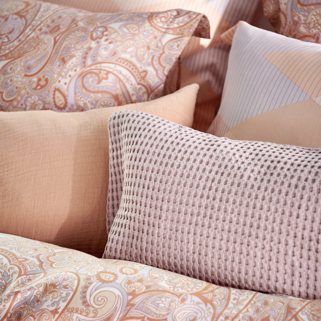 detail shot van een bed met kussens in oranje en lila pastel kleuren 