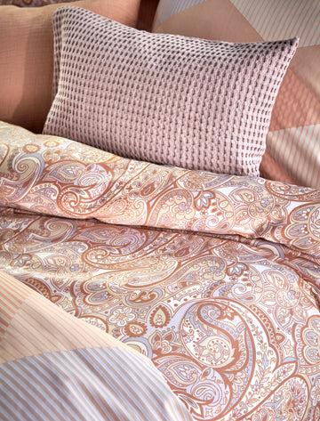 Een dekbedovertrek met paisley print en een sierkussen in paarse en oranje pastel kleuren